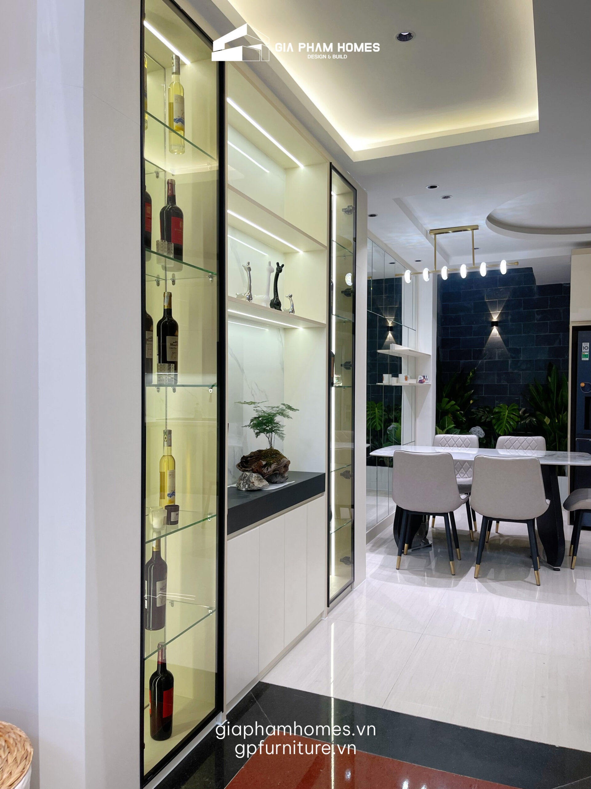 Tủ bếp Acrylic bóng gương: Sử dụng cốt gỗ MDF chống ẩm phủ Acrylic tông màu beige nhã nhặn. Bề mặt bóng gương không chỉ đẹp mà còn giúp gia chủ dễ dàng vệ sinh dầu mỡ.
Tủ rượu cánh kính: Hệ tủ rượu khung nhôm cánh kính tích hợp đèn LED vàng ấm là nơi trưng bày những chai rượu quý, nâng tầm đẳng cấp cho phòng ăn.